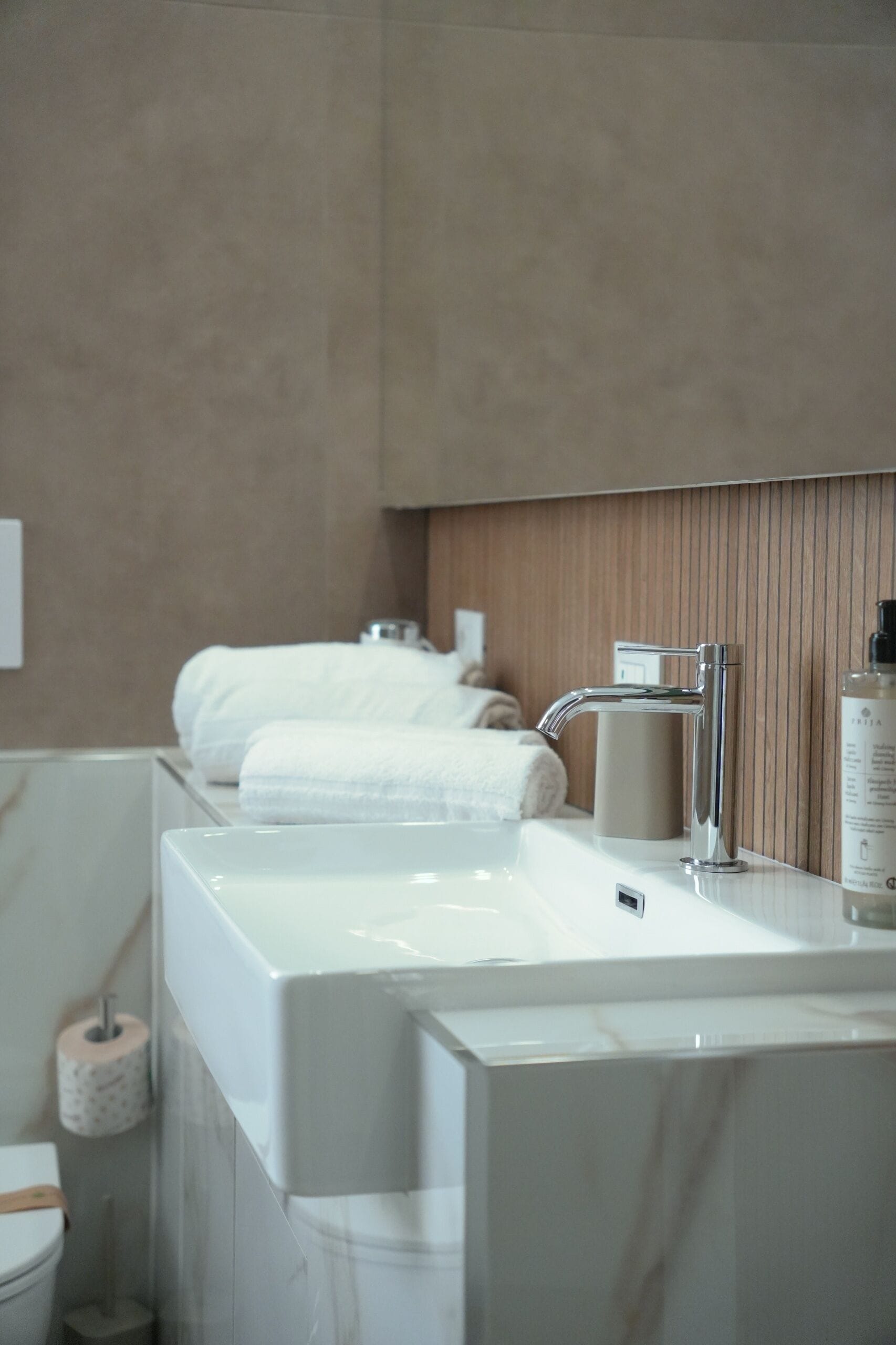 Un baño con un lavabo blanco, un grifo moderno y toallas ordenadas en una estantería.