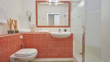 Un baño con inodoro blanco, lavabo, espejo y ducha.