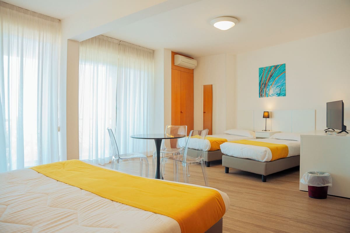 Habitación de hotel con cama, escritorio, silla, mesita, televisor y un cuadro en la pared.