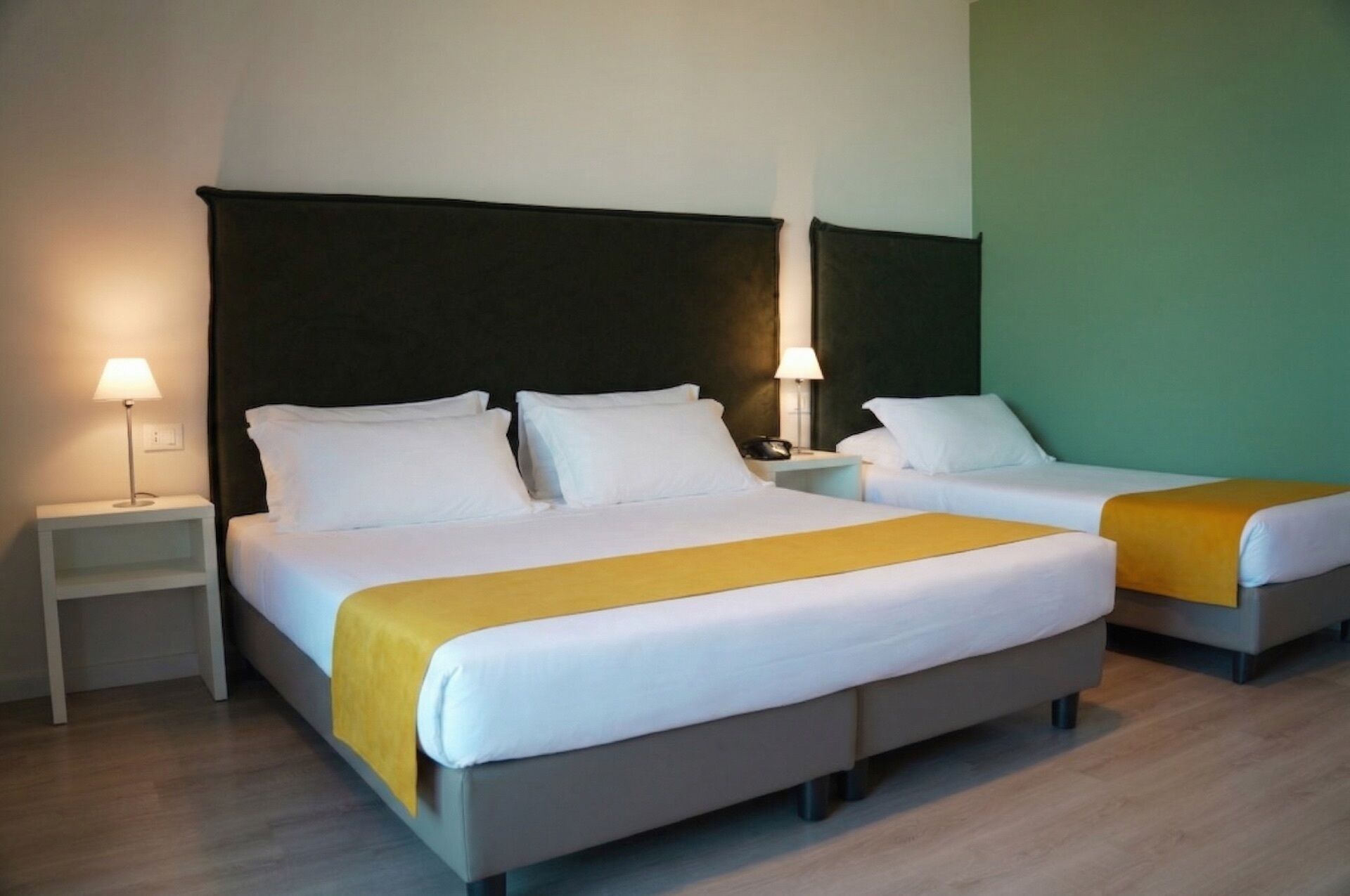 Ein Hotelzimmer mit zwei Betten, einem Nachttisch mit Lampe und einer grünen Wand.