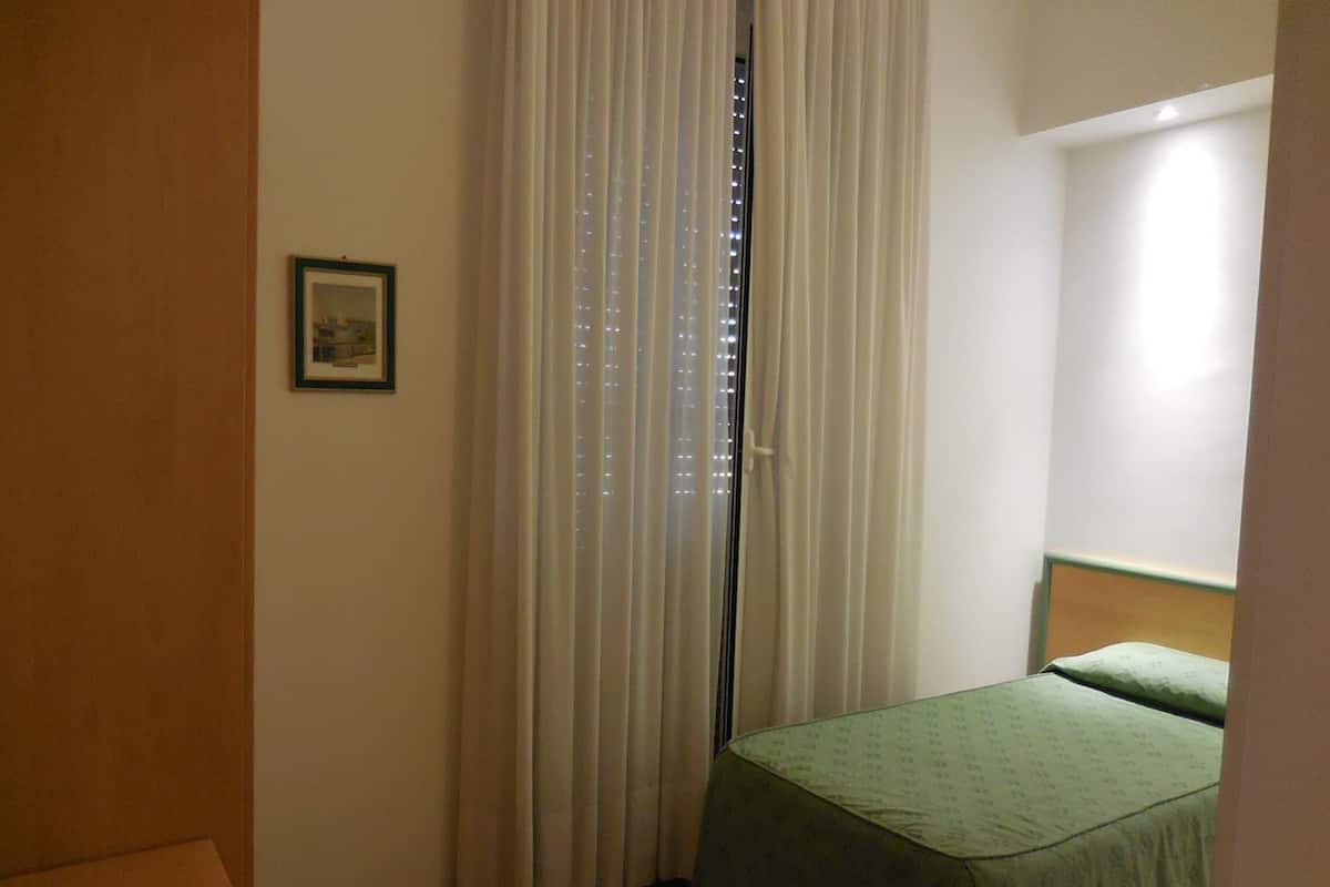 A small, simple room with a bed, a curtain, and a framed picture on the wall.