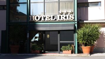 Un hotel chiamato "HOTEL IRIS" con una facciata moderna, ampie finestre e piante in vaso davanti.