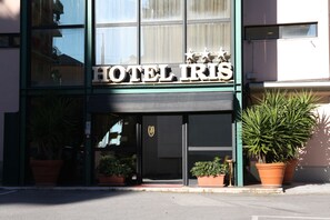 Un hotel llamado "HOTEL IRIS" con una fachada moderna, ventanas amplias y plantas en macetas al frente.
