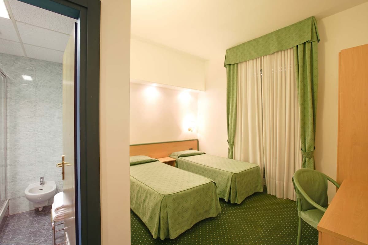 A hotel room with two single beds, a bathroom with a sink and toilet, and a green chair.