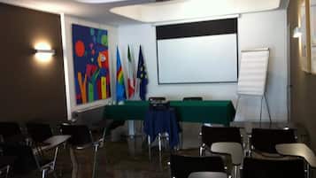 Una sala de conferències amb una pantalla de projector, una taula amb drap verd i diverses cadires.