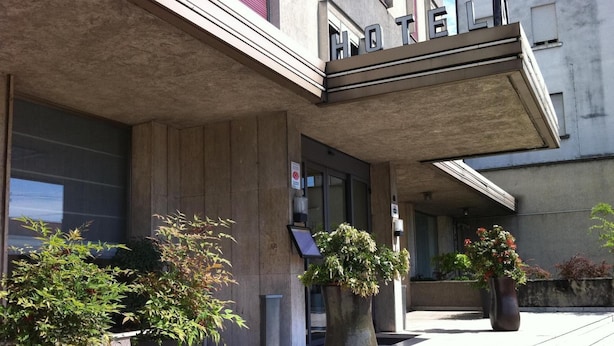 A hotel entrance with a concrete facade, large potted plants, and a sign indicating no smoking. - Hotel Al Cason (Padova)