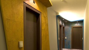 A hotel corridor with a carpeted floor, a wall-mounted elevator, and a door with a number. - Hotel Al Cason (Padova)