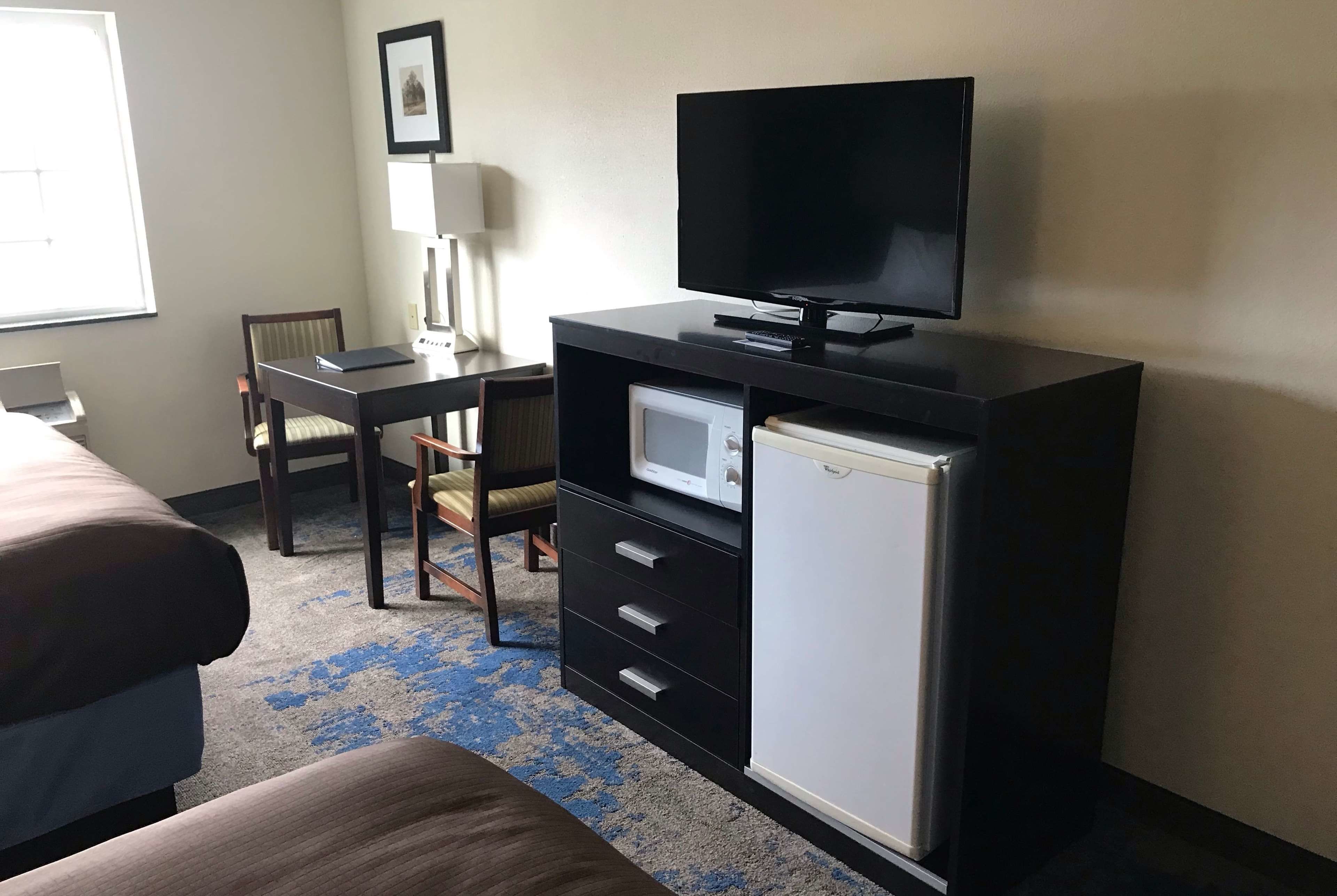 A hotel room with a bed, a desk with a computer, a television, a microwave, and a refrigerator.