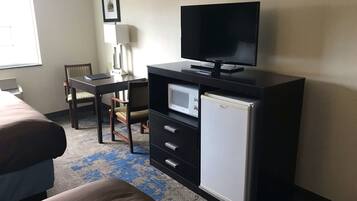 A hotel room with a bed, a desk with a computer, a television, a microwave, and a refrigerator.
