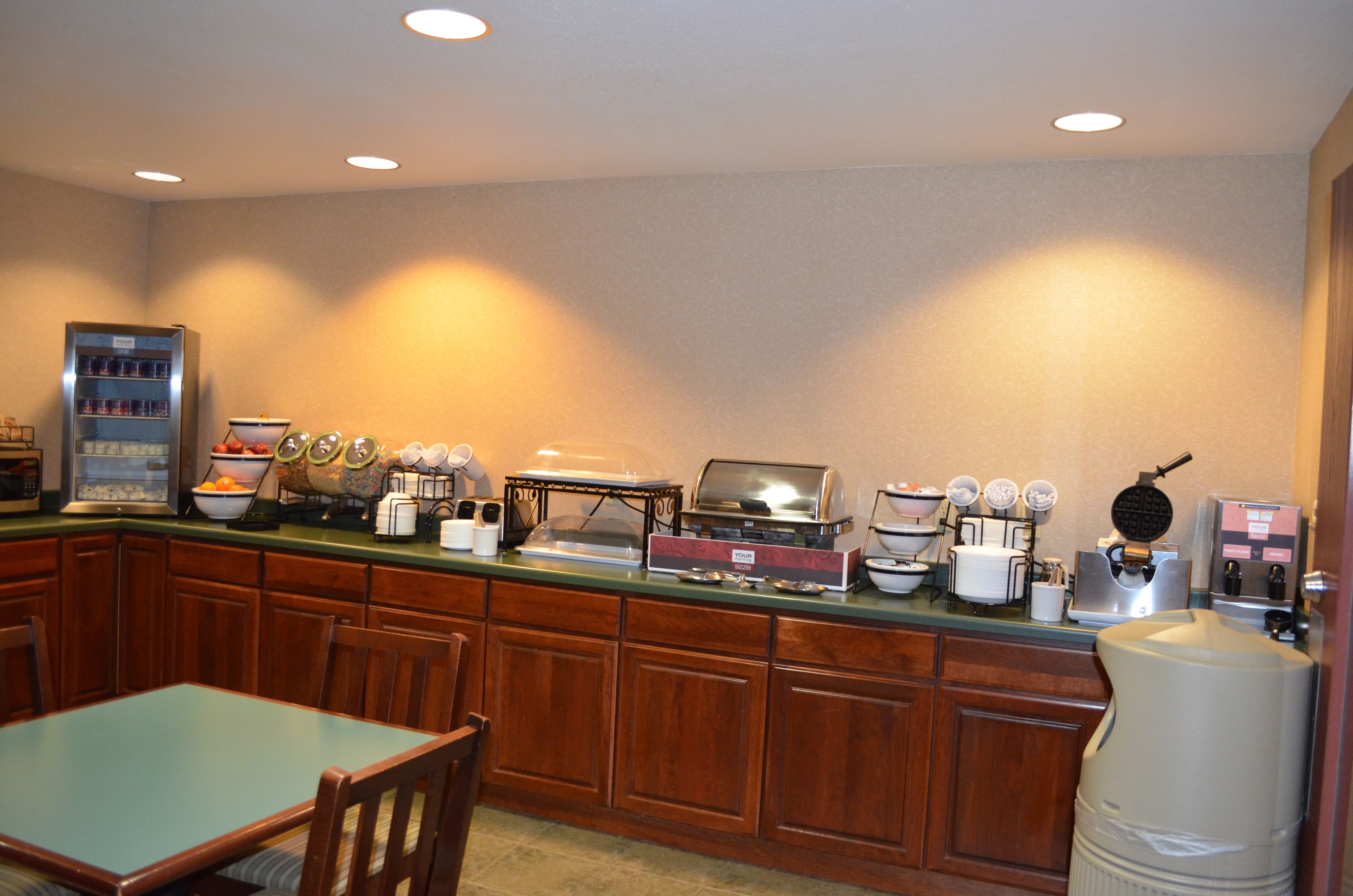 A breakfast bar with various appliances including a coffee maker, toaster, and waffle maker. There is a refrigerator and a microwave on the left, and a water dispenser on the right.