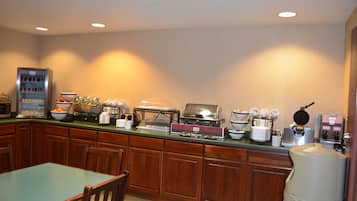 A breakfast bar with various appliances including a coffee maker, toaster, and waffle maker. There is a refrigerator and a microwave on the left, and a water dispenser on the right.