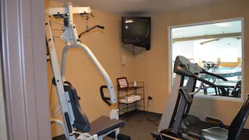 Et fitnessrum med træningsudstyr, et fjernsyn og et vindue med udsigt til udendørs siddepladser.