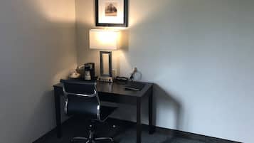 Een kleine kantoorruimte met een bureau, stoel, lamp en een ingelijst beeld aan de muur.