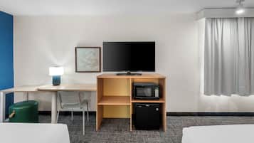 Habitación de hotel con cama, escritorio con lámpara, televisión, microondas y mini refrigerador.