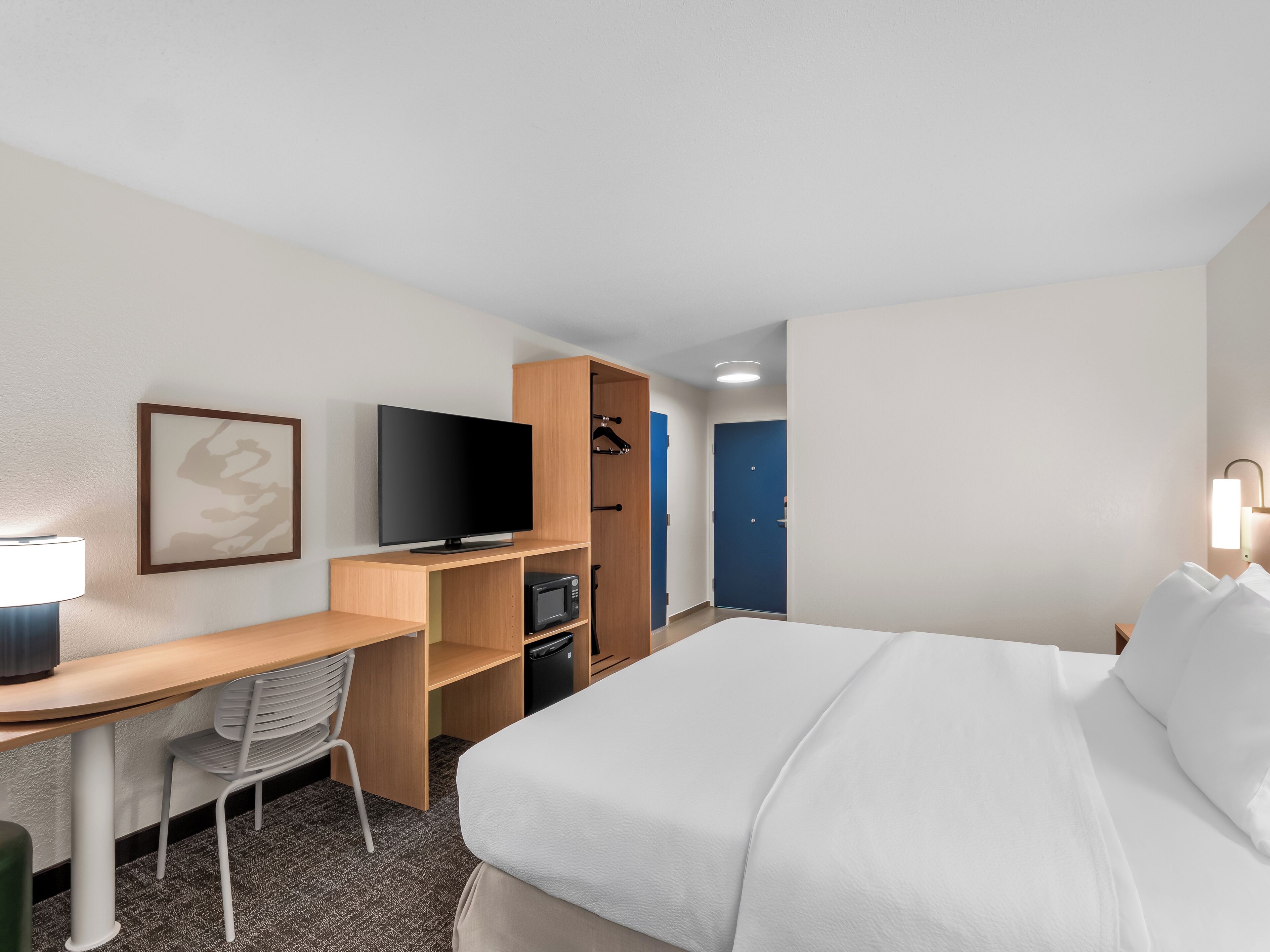 Een hotelkamer met een bed, bureau, stoel, televisie, kledingkast en een deur.