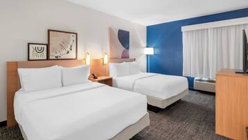 A hotel room with two beds, a desk, a TV, and artwork on the walls.