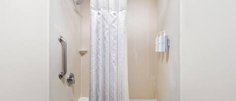 A bathroom with a shower, a handrail, a bathtub, and a wall-mounted soap dispenser.