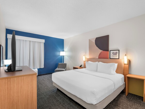 A hotel room with a large bed, a desk with a computer, a chair, a nightstand with a lamp, and a wall art piece. - Spark by Hilton Ann Arbor South (Ann Arbor)