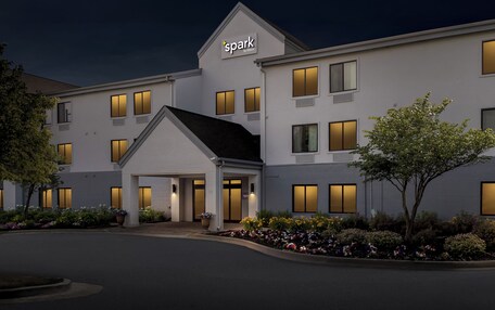 A hotel with a modern design, featuring a prominent 'spark by Hilton' sign, a covered entrance, and a well-maintained garden with various plants.