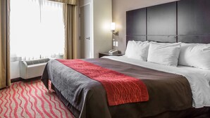 Habitación de hotel con una cama grande, una mesita de noche con lámpara, una ventana con cortinas y un aire acondicionado instalado en la pared.