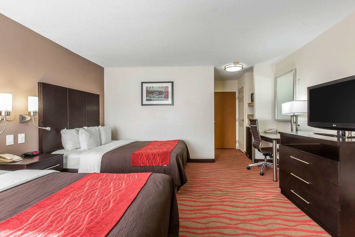 A hotel room with two beds, a desk, a television, and a bathroom visible in the background.