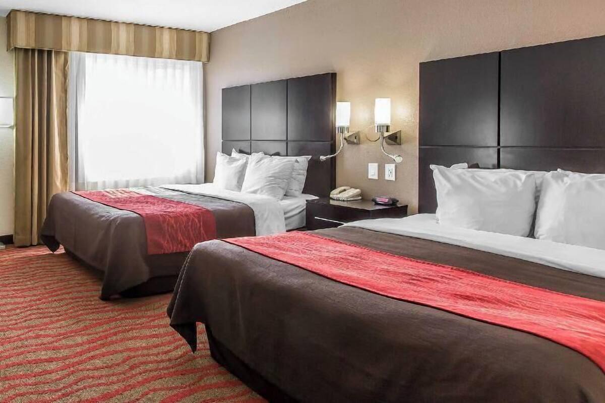 A hotel room with two beds, a red carpet, and a large window with curtains.