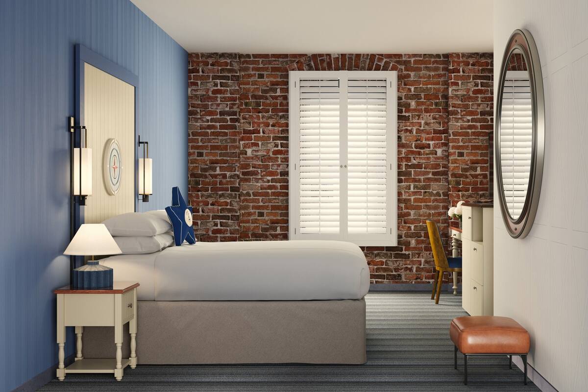 Een slaapkamer met een bakstenen muur, een bed, een nachtkastje met lamp, een dressoir, een stoel en een spiegel.