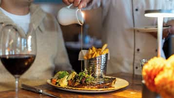 Ein Esstisch mit einem Teller Essen, einem Glas Rotwein und einer Metallbox mit Pommes.