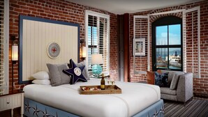 Une chambre d’hôtel avec un mur en briques, un lit sur lequel se trouve un plateau de nourriture, une lampe et une vue sur la ville par la fenêtre.
