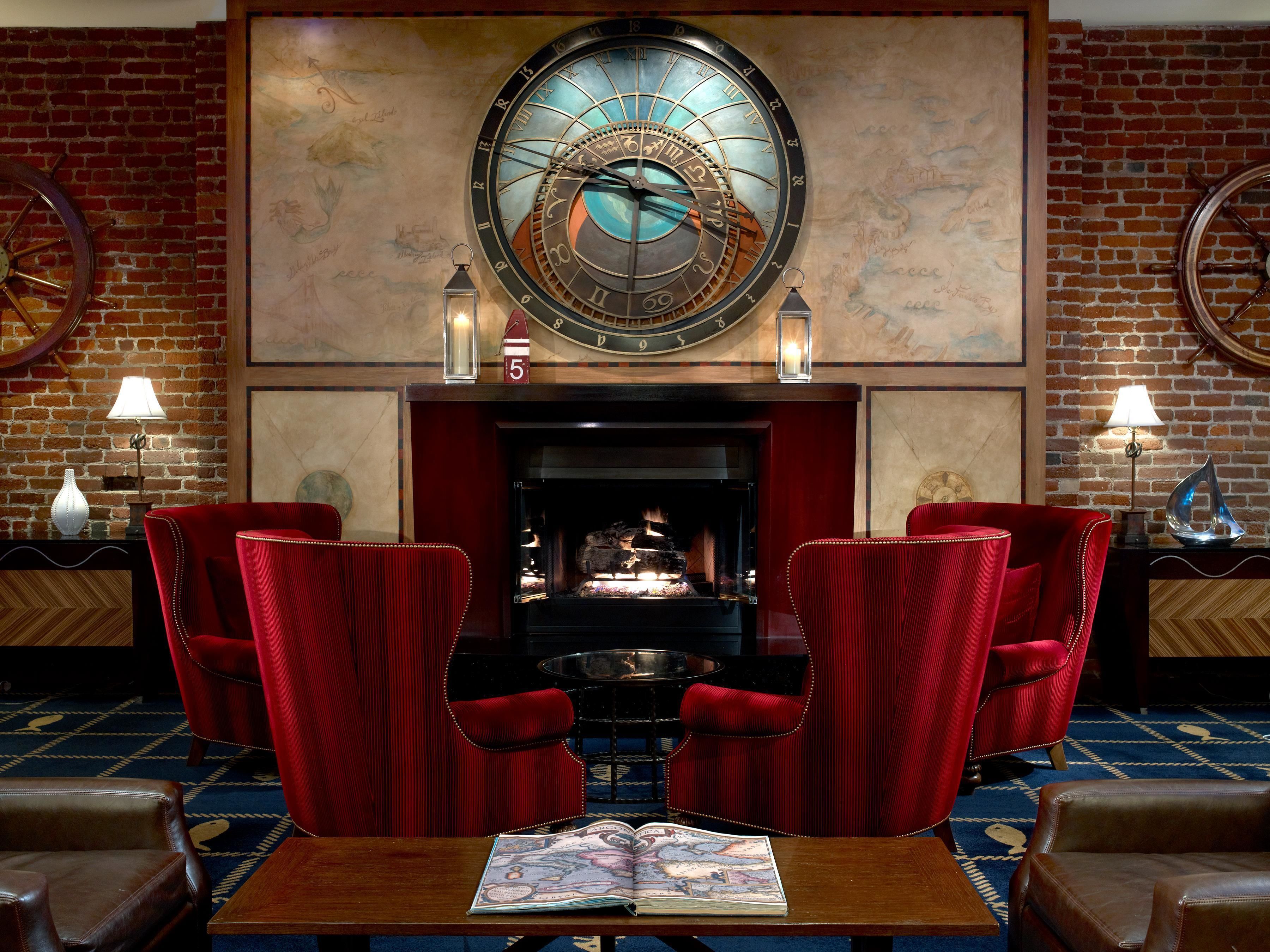 Une pièce avec une cheminée, des fauteuils à revêtement rouge, une horloge murale ronde et une carte accrochée au mur.
