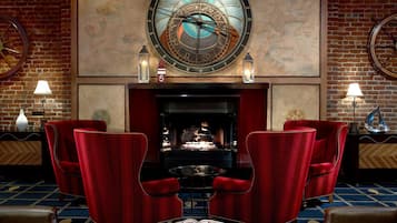 Une pièce avec une cheminée, des fauteuils à revêtement rouge, une horloge murale ronde et une carte accrochée au mur.