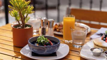A dining table with a potted plant, a bowl of salad, a glass of orange juice, and a plate with pancakes.
