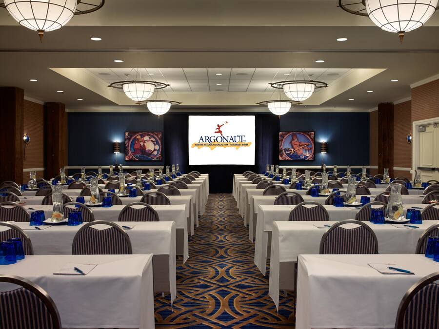A conference room with rows of tables, chairs, and a large screen displaying the Argonaut logo.