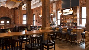 Un vaste espace bar agrémenté de poutres en bois apparentes, d’un mur en briques et de différents types de sièges, notamment des tabourets de bar et des tables.