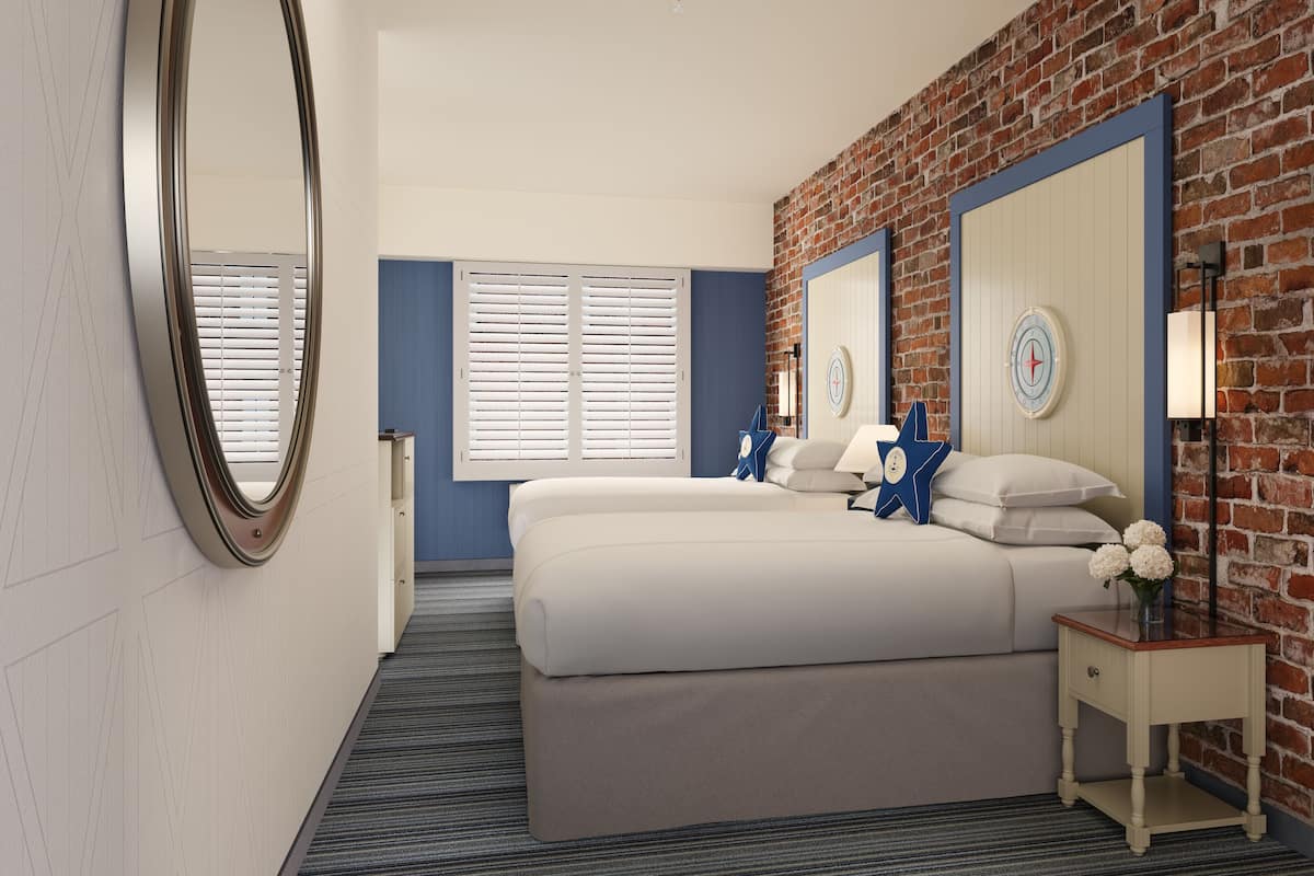 Een hotelkamer met een bakstenen muur, een groot bed met wit beddengoed, een nachtkastje met een lamp en een spiegel.