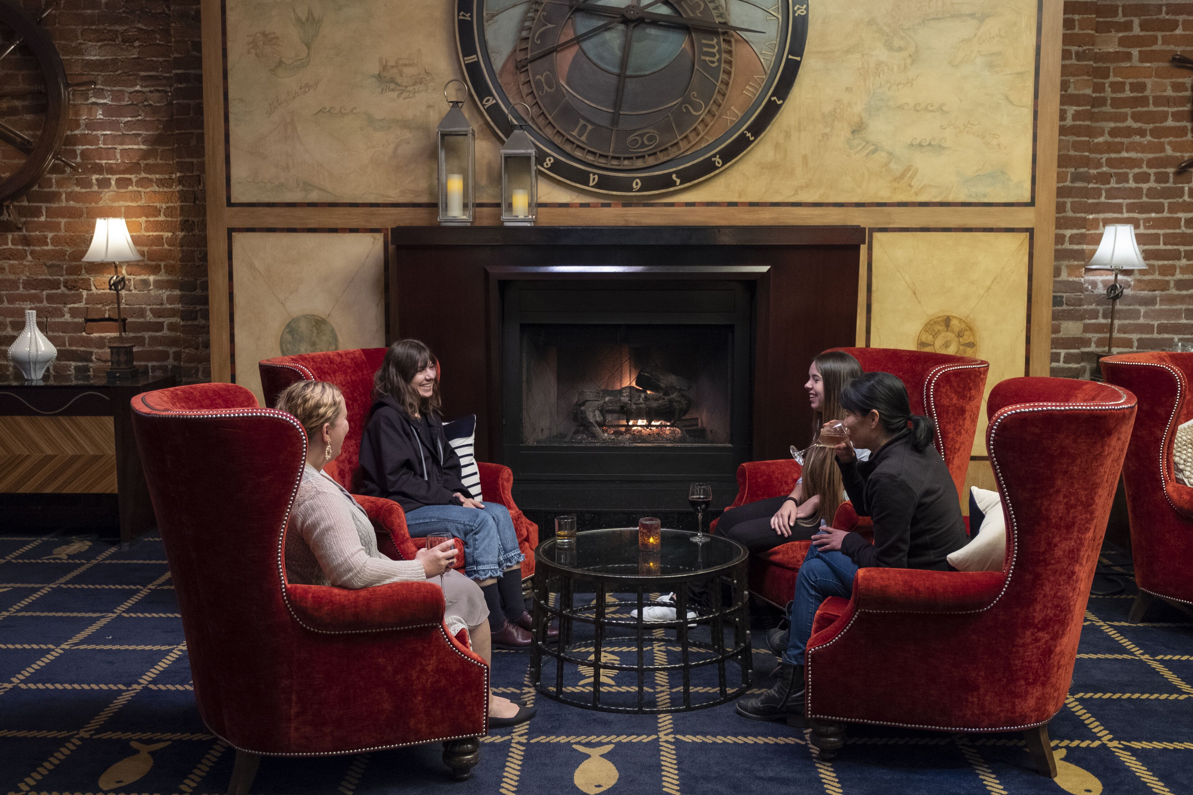 A cozy lounge area with red upholstered chairs, a round table, and a fireplace.