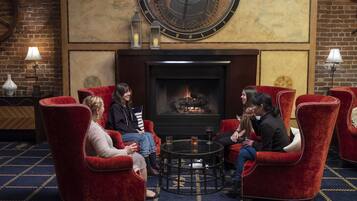 A cozy lounge area with red upholstered chairs, a round table, and a fireplace.