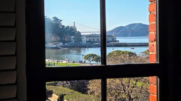 A view through a window of a building with a brick wall, a park with benches, and a body of water with boats and a bridge in the distance.
