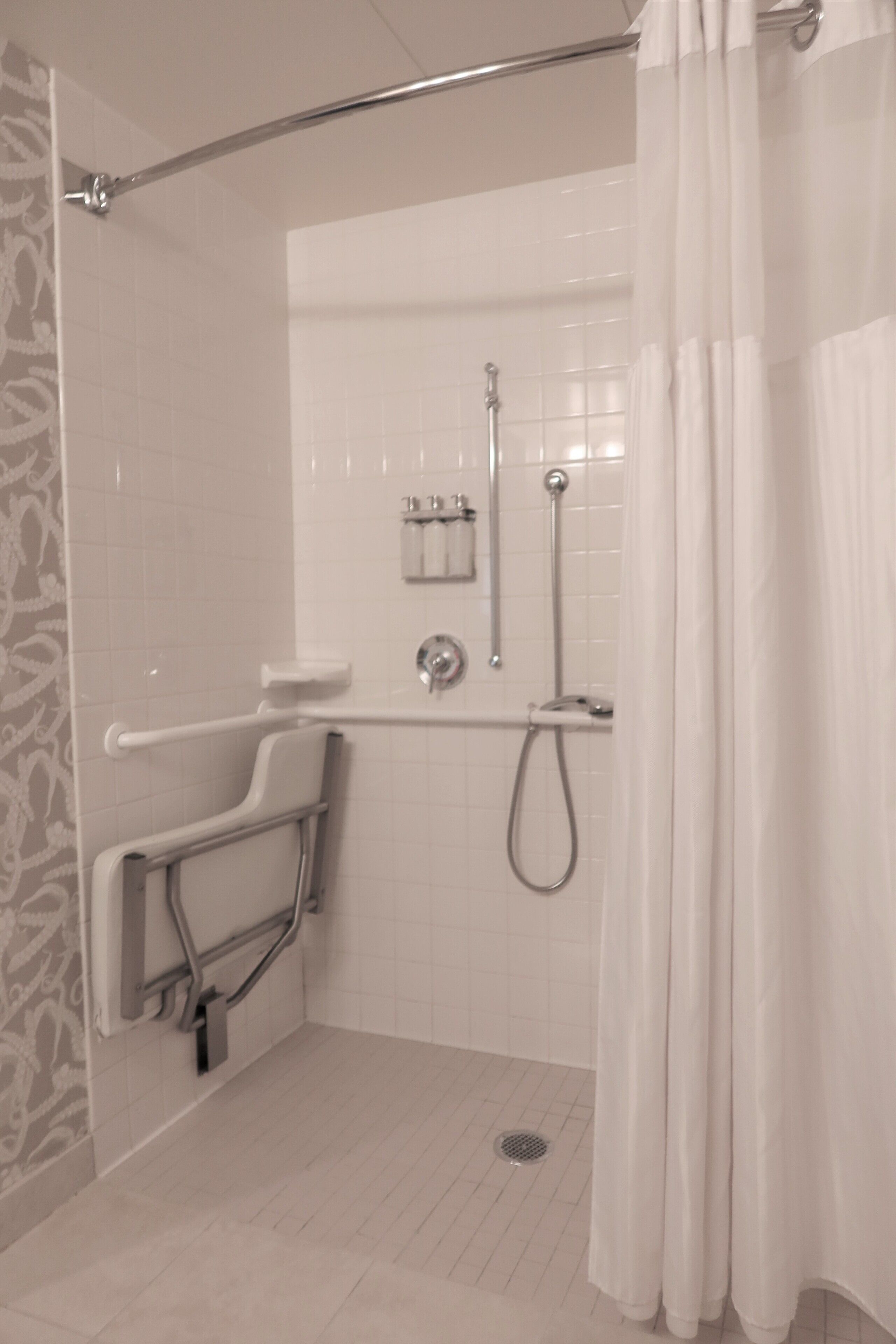 A bathroom with a shower, grab bars, a toilet, and a hand dryer.