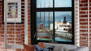 A room with a large window overlooking a harbor, featuring a sailboat and a building with multiple stories.