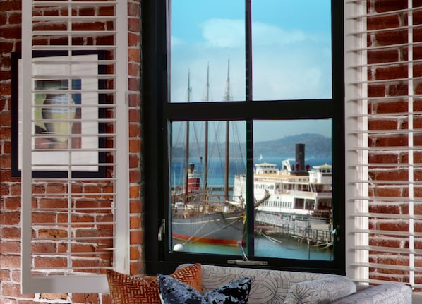 Una habitación con un ventanal grande que da a un puerto, con un velero y un edificio de varios pisos.