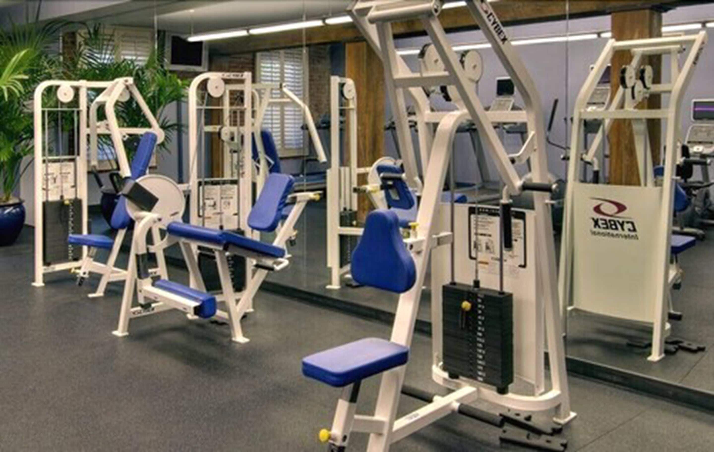Ein Fitnessraum mit verschiedenen Trainingsgeräten, darunter eine Beinpresse und eine Brustpresse.