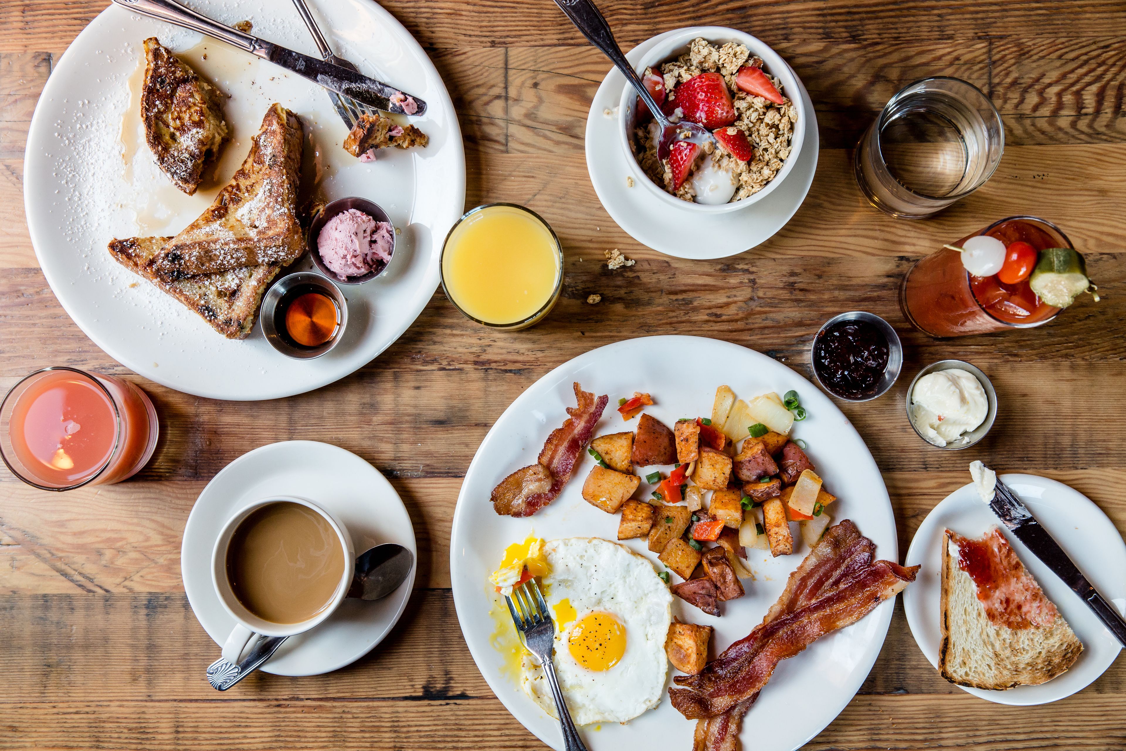 Una mesa de desayuno con diversos platos, entre ellos huevos, tocino, tostadas y fruta.