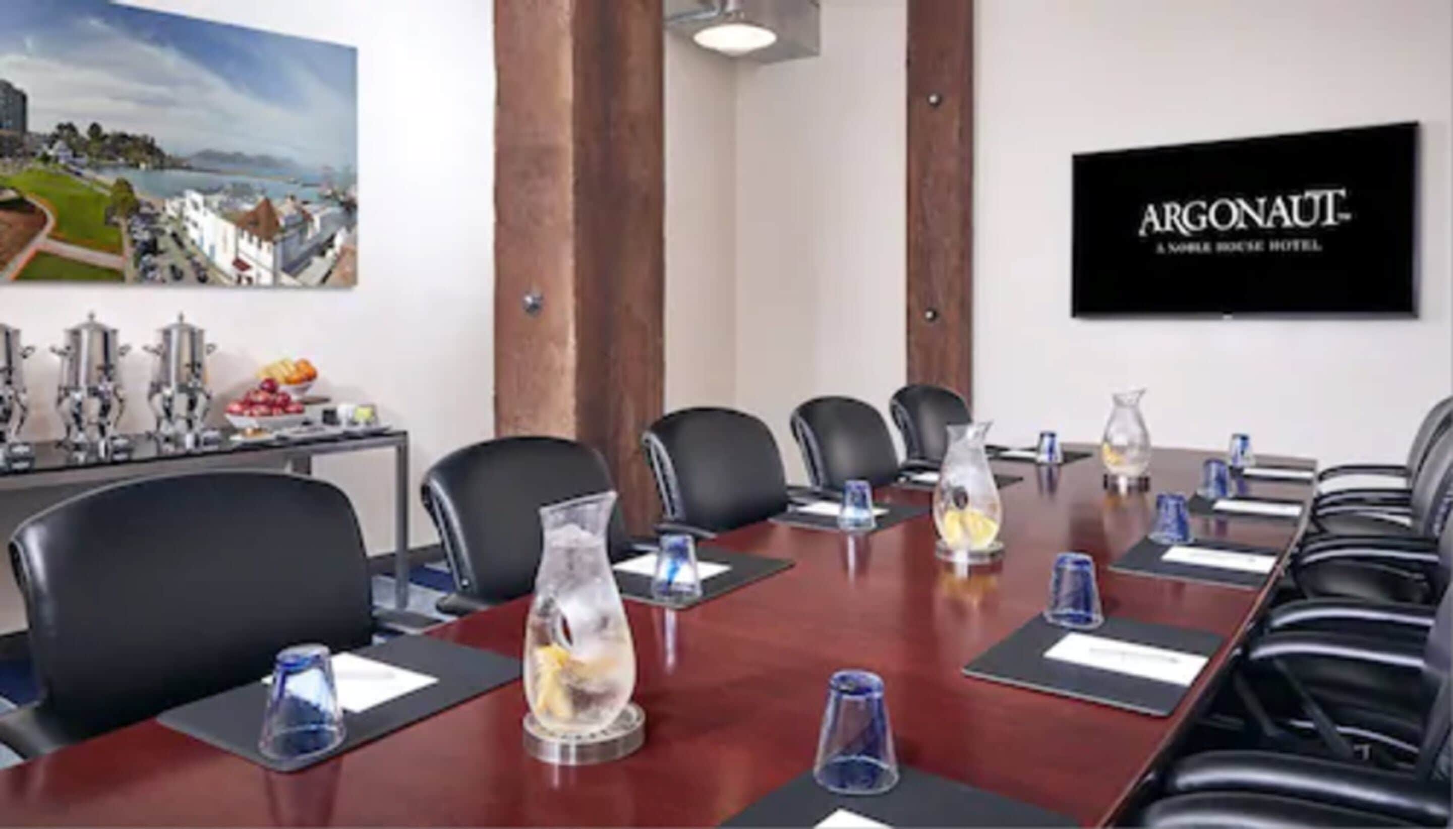 A conference room with a long table, black chairs, and a painting of a coastal scene.