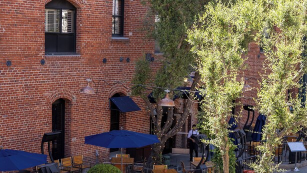 Un café en plein air avec des murs en briques, des tables à l’extérieur et un arbre au premier plan.