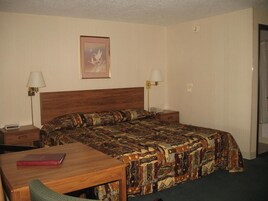 A hotel room with a wooden bed, two bedside tables, a desk with a chair, a patterned bedspread, and a framed picture on the wall.