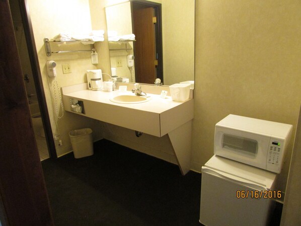 Une salle de bain d’hôtel équipée d’un lavabo, d’un miroir, d’un porte-serviettes, d’un sèche-cheveux et d’un four à micro-ondes.