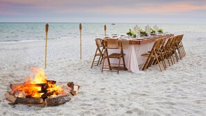 Un espacio para comer frente al mar, con un brasero, sillas de madera y una mesa dispuesta para una comida.
