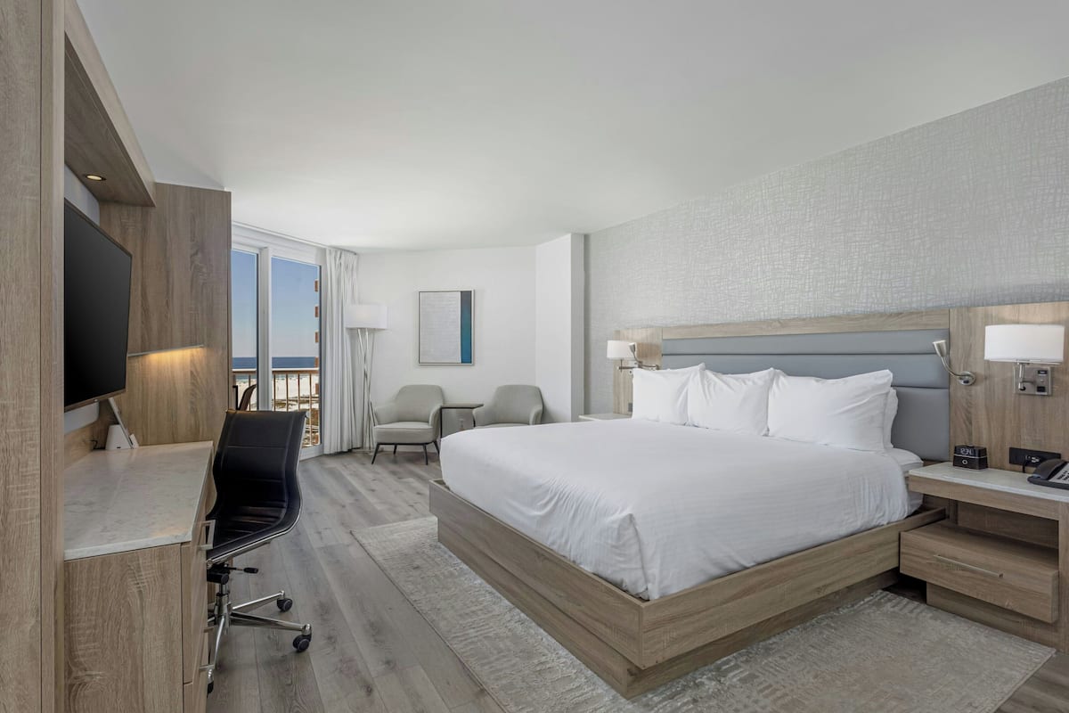 A hotel room with a bed, desk, chairs, and a TV.