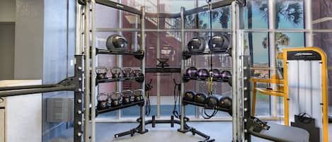 A gym with weightlifting equipment, kettlebells, and a bench.